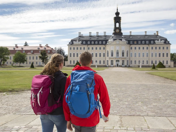 Pohled zezadu na dvojici při pohledu na zámek Hubertusburg ve Wermsdorfu, modrá obloha, mraky