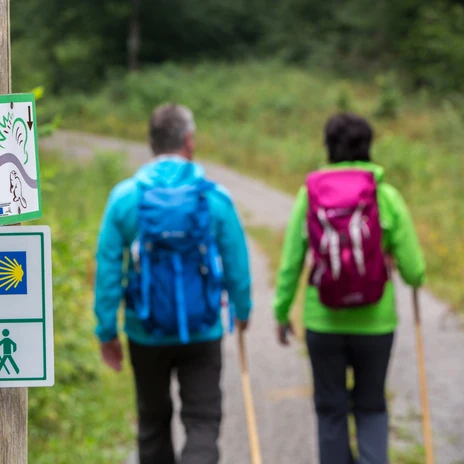 Značka s nápisem Lutherweg, za ní dvojice v turistickém oblečení v šmouze