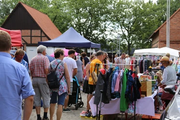 Flohmarkt-Steinhude-Sievers Menschen stöbern bei sonnigem Wetter durch einen lebhaften Flohmarkt mit bunten Ständen und Kleidung.