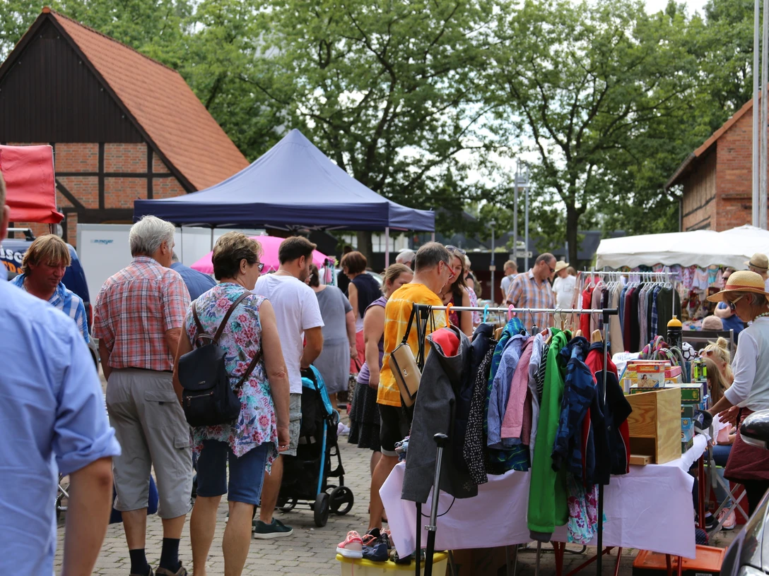 Flohmarkt-Steinhude-Sievers Menschen stöbern bei sonnigem Wetter durch einen lebhaften Flohmarkt mit bunten Ständen und Kleidung.