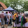 Flohmarkt-Steinhude-Sievers Menschen stöbern bei sonnigem Wetter durch einen lebhaften Flohmarkt mit bunten Ständen und Kleidung.