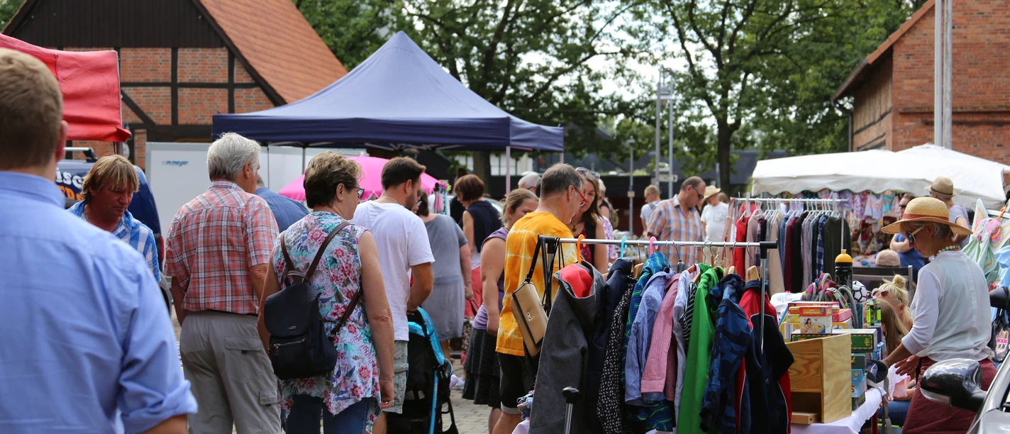 Flohmarkt-Steinhude-Sievers Menschen stöbern bei sonnigem Wetter durch einen lebhaften Flohmarkt mit bunten Ständen und Kleidung.