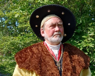 Edzard I. "der große" Cirksena Mann in historischer Kleidung mit Pelzkragen und großem Hut vor grünem Hintergrund im Freien.