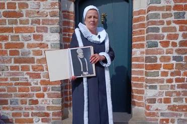 Gräfin Anna von Ostfriesland Frau in historischer Tracht hält ein Porträt von Gräfin Anna von Ostfriesland vor Backsteinmauer.