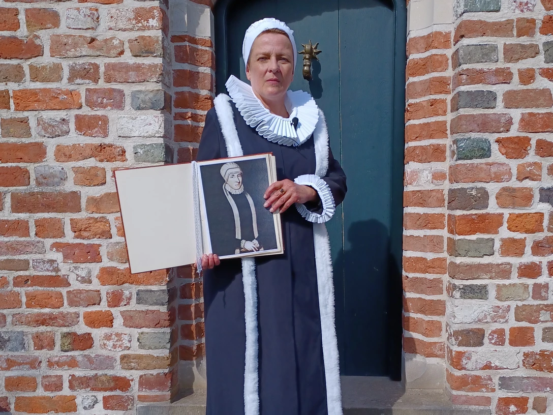 Gräfin Anna von Ostfriesland Frau in historischer Tracht hält ein Porträt von Gräfin Anna von Ostfriesland vor Backsteinmauer.