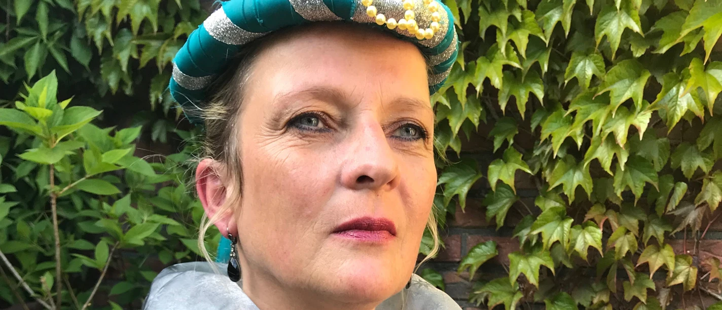 LAK: Der letzte Häuptling - Der Mann von Gräfin Theda Frau in historischem Kostüm mit türkis-silberner Haube und besticktem Kleid vor grüner Efeuwand.