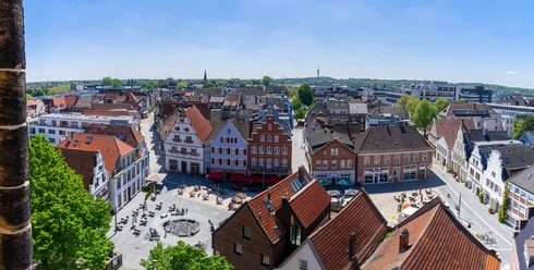 Rheine_Marktplatz03_Bildrechte EWG Rheine.jpg Panorama des belebten Marktplatzes in Rheine mit historischen Gebäuden und Menschen im Freien.
