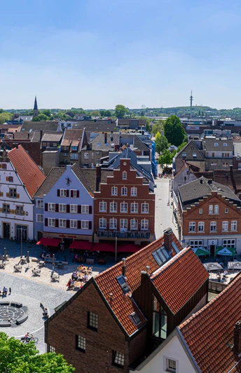 Rheine_Marktplatz03_Bildrechte EWG Rheine.jpg Panorama des belebten Marktplatzes in Rheine mit historischen Gebäuden und Menschen im Freien.