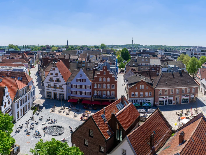 Rheine_Marktplatz03_Bildrechte EWG Rheine.jpg Panorama des belebten Marktplatzes in Rheine mit historischen Gebäuden und Menschen im Freien.