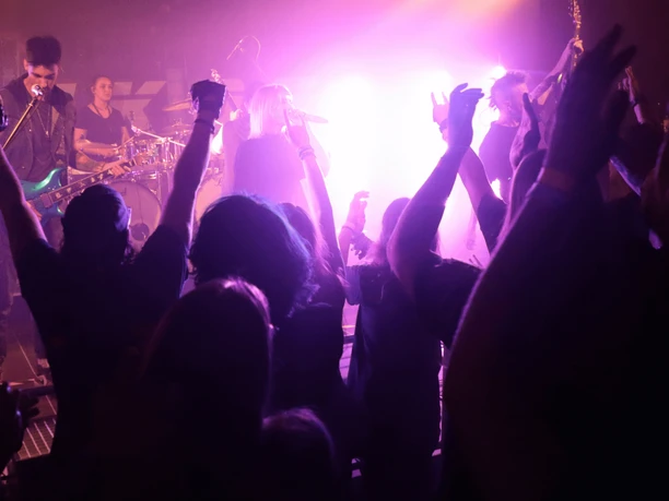 Druckerei Indoor Menschen jubeln und tanzen vor einer Bühne bei einem Konzert mit farbigen Lichteffekten.