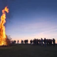 Großes Feuer lodert in der Abenddämmerung, umgeben von Menschen, die den traditionellen Brauch beobachten.