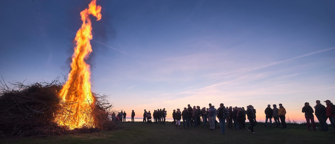 Osterfeuer Großes Feuer lodert in der Abenddämmerung, umgeben von Menschen, die den traditionellen Brauch beobachten.