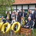 VolkschorGehlenbeck.JPG Mitglieder des Volkschors Gehlenbeck feiern vor einem Fachwerkhaus ein Jubiläum mit goldenen Luftballons.