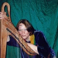 Harfenistin Gertraude Büttner Harfenistin Gertraude Büttner lächelnd in traditioneller Kleidung vor einem grünen Hintergrund mit Harfe.