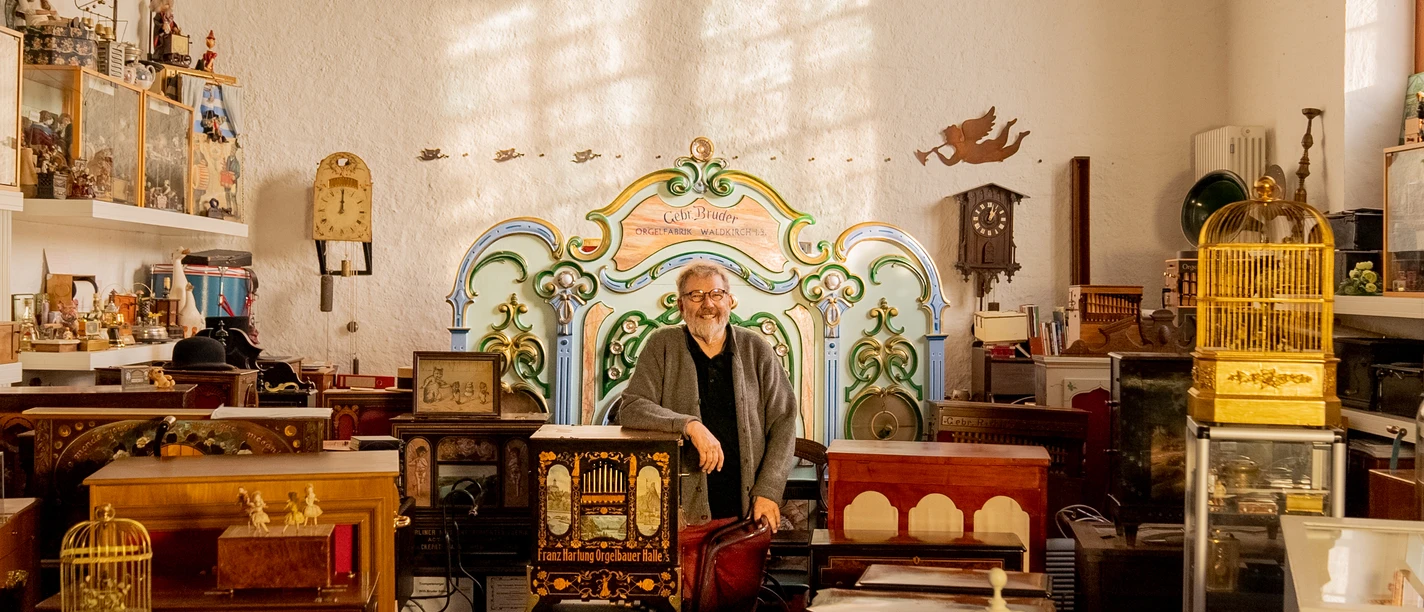 Drehorgelmuseum Ein Mann steht in einem Raum voller antiker Musikautomaten und Orgeln, umgeben von nostalgischer Stimmung.