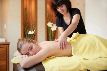 Een vrouw krijgt een rugmassage op een tafel bedekt met een gele handdoek; de sfeer is ontspannend.
