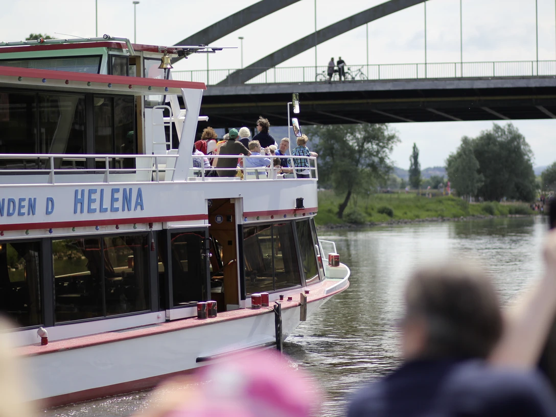 Mindener Fahrgastschiffahrt - Helena Das Fahrgastschiff Helena auf der Weser, im Hintergrund eine Brücke und grüne Uferbereiche.