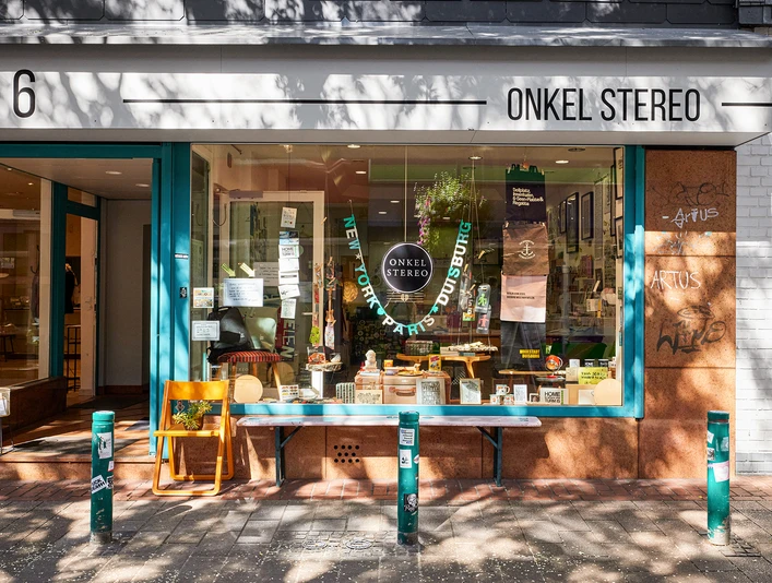 Oom Stereo buitenaanzicht, Duisburg Vorderseite des Cafés "Onkel Stereo" in Duisburg mit einer einladenden Glasfassade und buntem Interieur.Front of the “Onkel Stereo” café in Duisburg with an inviting glass façade and colorful interior.Voorkant van het “Onkel Stereo” café in Duisburg met een uitnodigende glazen gevel en kleurrijk interieur.
