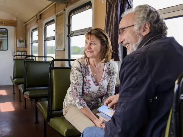 Excursion on the "Wilder Robert" narrow-gauge railroad - Holidays in the Leipzig region A couple sits smiling on the Wilder Robert narrow-gauge railroad in the Leipzig region, the man holding a brochure