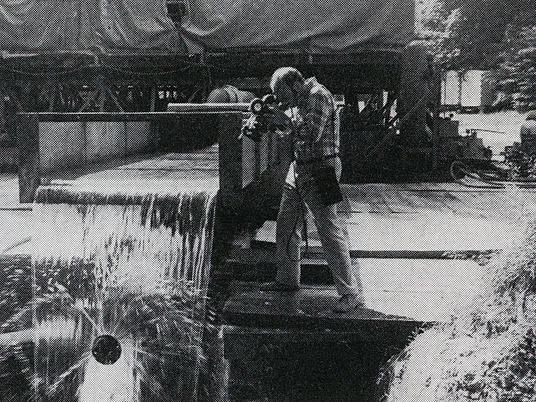 Alexander-von-Humboldt-Quelle Ein Mann fotografiert die sprudelnde Alexander-von-Humboldt-Quelle inmitten einer bewaldeten Umgebung.