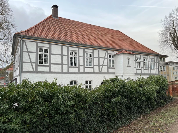 Amtshaus Fachwerkgebäude mit roten Dachziegeln und weißen Wänden von einer grünen Hecke umgeben.