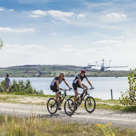 Deux cyclistes sur route au bord du lac de Markkleeberg, dans la région de Leipzig : piste cyclable, lac, nature, ciel bleu, nuages, grue