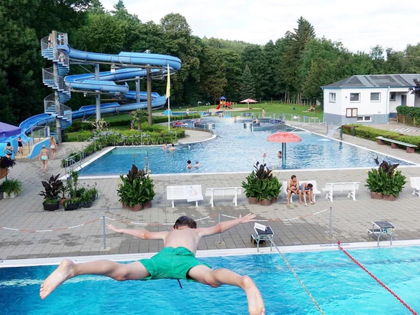 Berggießhübel open-air swimming pool A young man splashes into the water of an outdoor pool with slides and swimmers in summer fun.