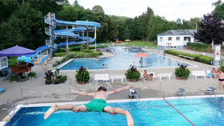 Freibad Berggießhübel Ein junger Mann spritzt ins Wasser eines Freibads mit Rutschen und Schwimmern im Sommervergnügen.