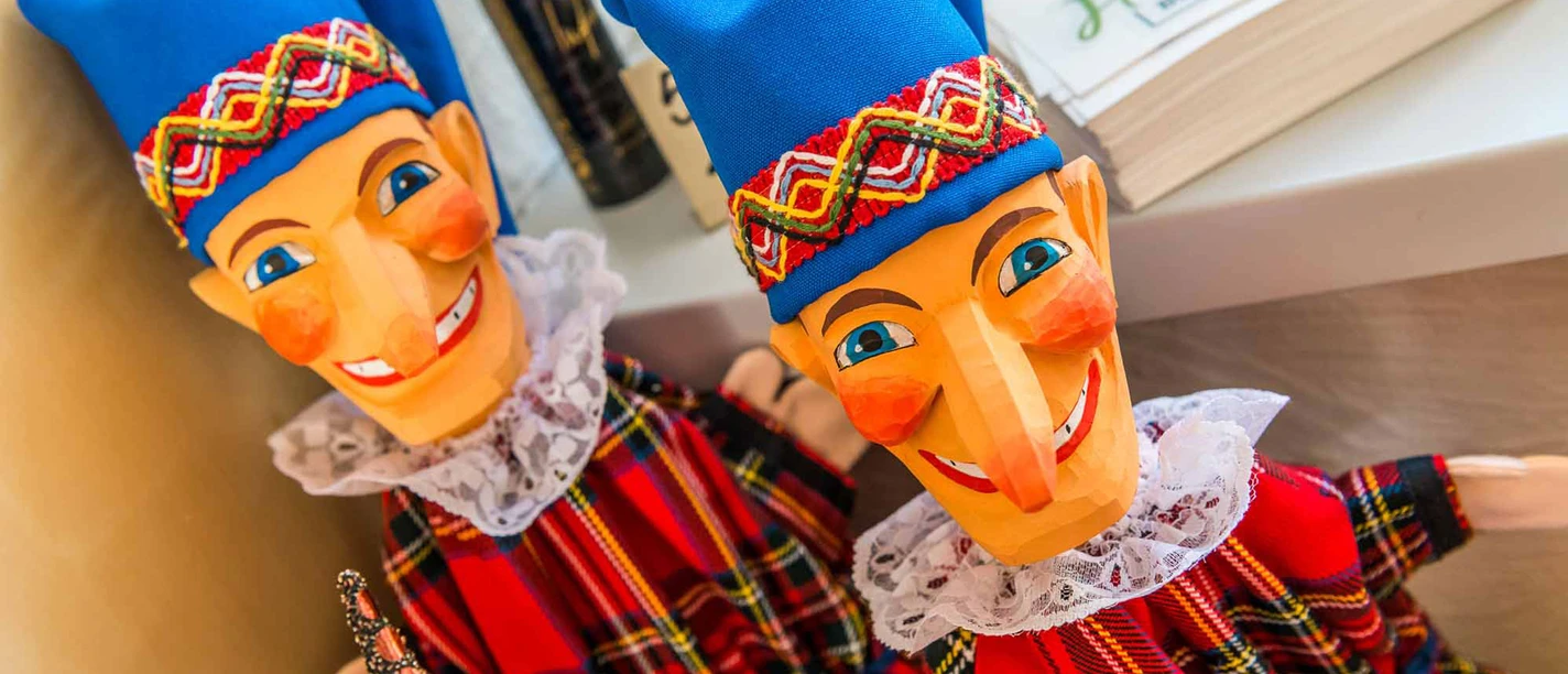 Two colorful Punch and Judy figures with blue caps and checkered dresses stand next to each other on a shelf, smiling happily.