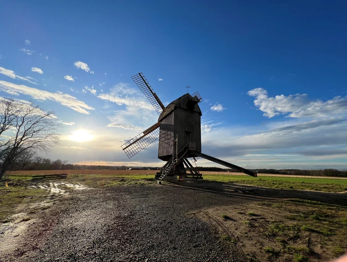 Mühle Neuenknick Historische, hölzerne Windmühle auf einem Feld bei Sonnenuntergang, umgeben von weitem Himmel und Wolken.