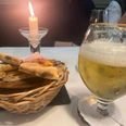 Ein Glas Bier und ein Brotkorb stehen auf einem Tisch, sanft beleuchtet von einer Kerze.