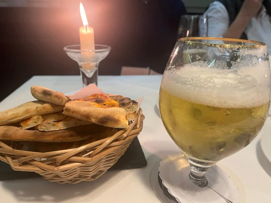 Ein Glas Bier und ein Brotkorb stehen auf einem Tisch, sanft beleuchtet von einer Kerze.