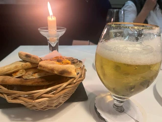 Brot und Bier_CCBYSA_Teutoburger Wald_Stadt Schloss Holte-Stukenbrock-12.jpg Ein Glas Bier und ein Brotkorb stehen auf einem Tisch, sanft beleuchtet von einer Kerze.