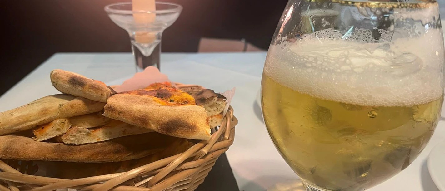 Ein Glas Bier und ein Brotkorb stehen auf einem Tisch, sanft beleuchtet von einer Kerze.