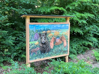 Informationstafel im Wald mit naturgetreuem Bild von Wildschwein, Wildkatze und Eule umrahmt von Bäumen.