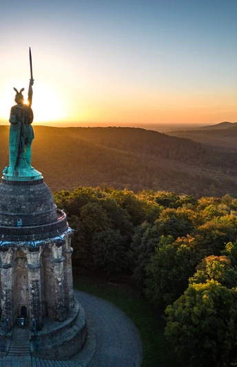 Hermannsdenkmal im Teutoburger Wald bei Sonnenuntergang, umgeben von dichten Wäldern und sanften Hügeln.