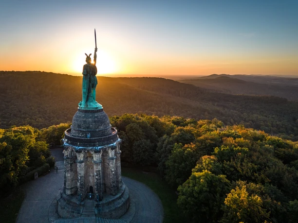 Detmold-Hermannsdenkmal-Teutoburger-Wald-Tourismus-D-Ketz-099.jpg Hermannsdenkmal im Teutoburger Wald bei Sonnenuntergang, umgeben von dichten Wäldern und sanften Hügeln.