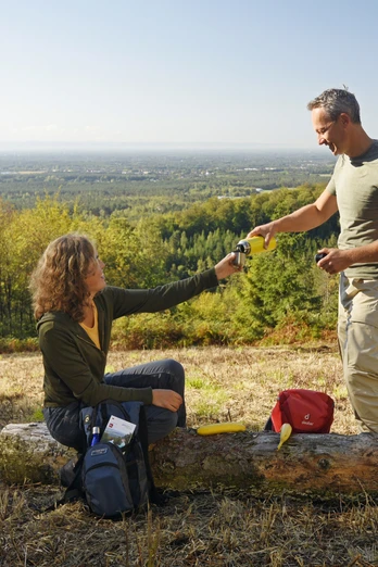 Oerlinghausen-Ausblick-ins-Lipperland-Teutoburger-Wald-Tourismus-F-Grawe (64).JPG Zwei Personen auf einer Lichtung im Teutoburger Wald, tauschen Getränke mit bewaldetem Lipperland im Hintergrund.
