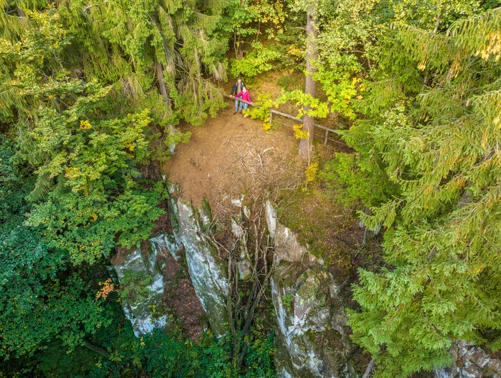 Ein Wanderer sitzt auf einer Bank am bewaldeten Rand eines Felsvorsprungs im Teutoburger Wald.