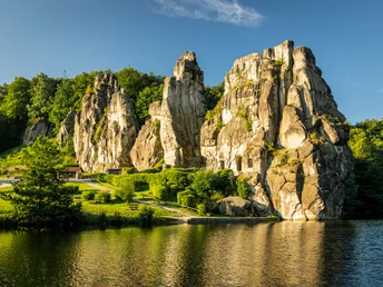 Externsteine Horn-Bad Meinberg Felsenformation Externsteine erhebt sich imposant aus grüner Landschaft, umgeben von ruhigem Wasser.