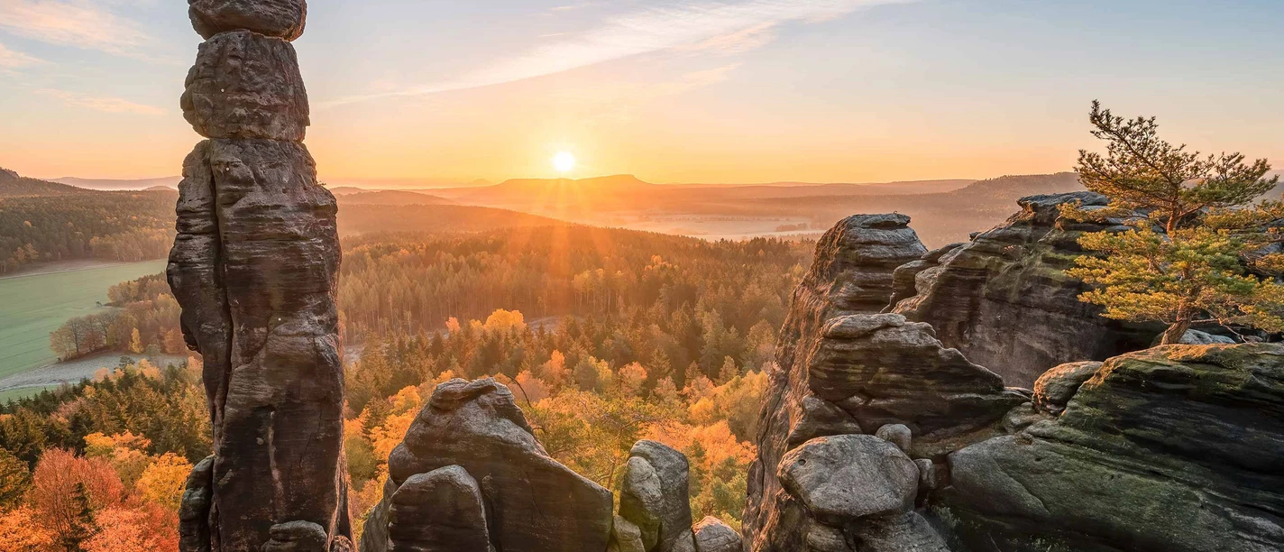Barbarine on the Pfaffenstein Rock formations called Barbarine at sunrise, surrounded by autumn-colored forests; clear, peaceful atmosphere with a bright sky.