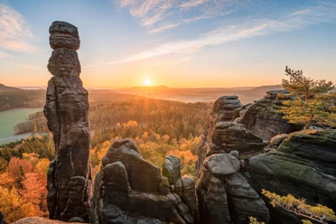 Barbarine op de Pfaffenstein Rotsformaties genaamd Barbarine bij zonsopgang, omgeven door herfstkleurige bossen; heldere, vredige sfeer met een heldere hemel.