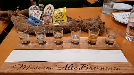 Sechs Schnapsgläser auf einem Holzkastl mit der Aufschrift "Museum Alte Brennerei", Tasting-Set.