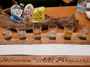 Korn Tasting - alte Brennerei Hille Sechs Schnapsgläser auf einem Holzkastl mit der Aufschrift "Museum Alte Brennerei", Tasting-Set.