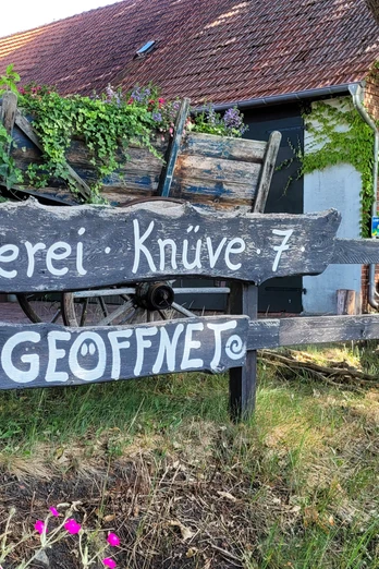 Töpferei im Grünen mit rustikaler Holzbeschilderung, Wagenrad und üppiger Efeubewachsung.