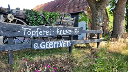 Keramikwerkstatt Sundern Töpferei im Grünen mit rustikaler Holzbeschilderung, Wagenrad und üppiger Efeubewachsung.