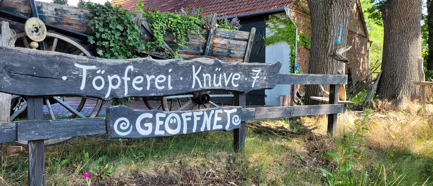 Keramikwerkstatt Sundern Töpferei im Grünen mit rustikaler Holzbeschilderung, Wagenrad und üppiger Efeubewachsung.