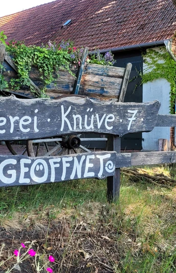 Keramikwerkstatt Sundern Töpferei im Grünen mit rustikaler Holzbeschilderung, Wagenrad und üppiger Efeubewachsung.