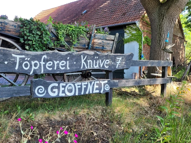 Keramikwerkstatt Sundern Töpferei im Grünen mit rustikaler Holzbeschilderung, Wagenrad und üppiger Efeubewachsung.