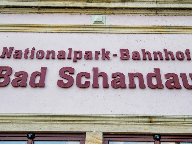 Nationalparkbahnhof Bad Schandau Rote Schrift auf rosa Wand mit der Aufschrift "Nationalpark-Bahnhof Bad Schandau".